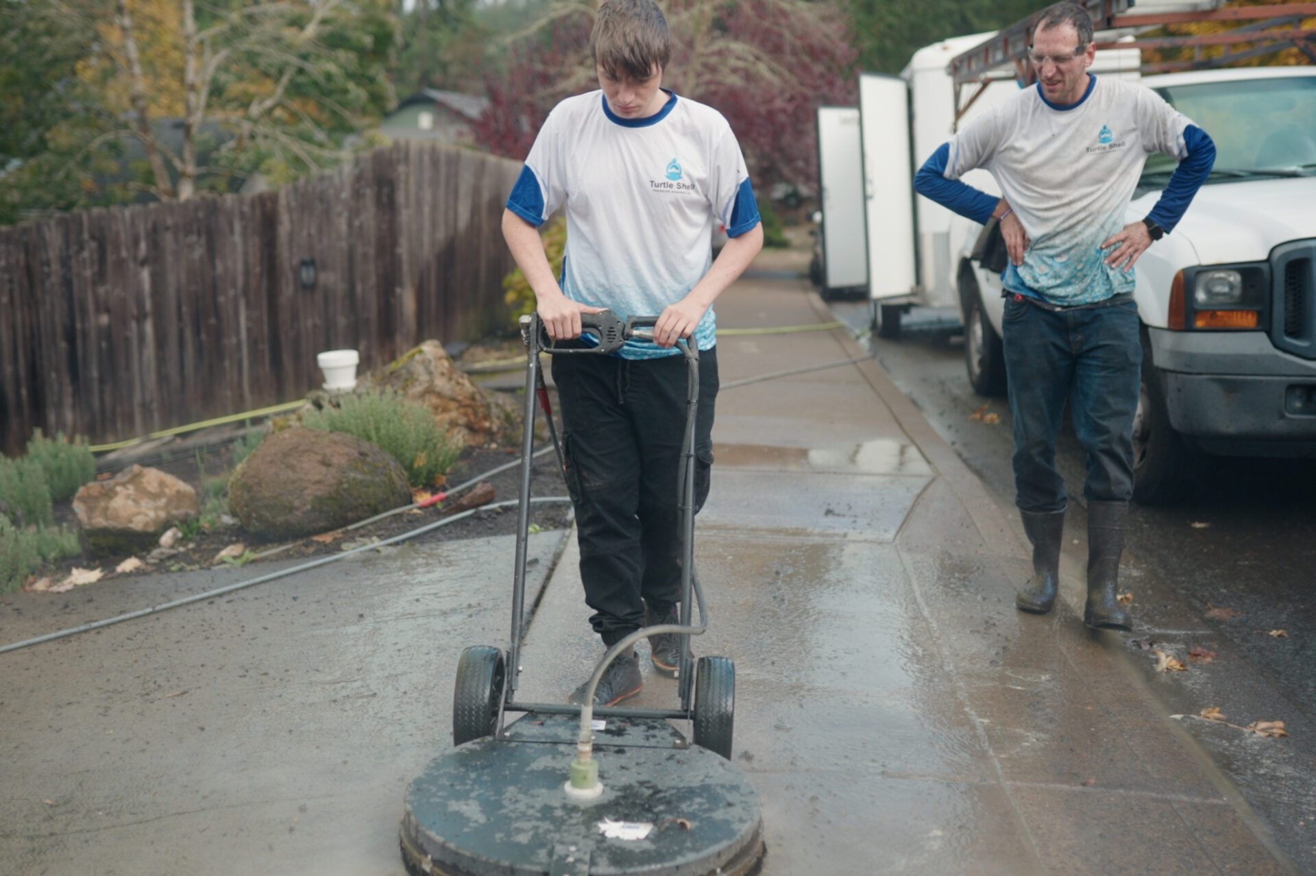 Two individuals power washing a driveway